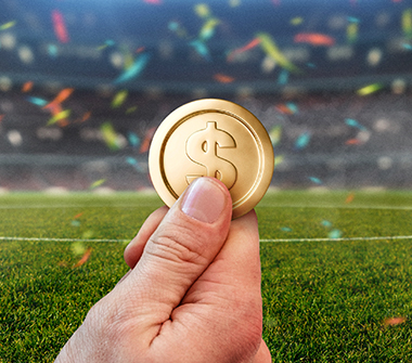 Hand holding coin in sports field with confetti falling.