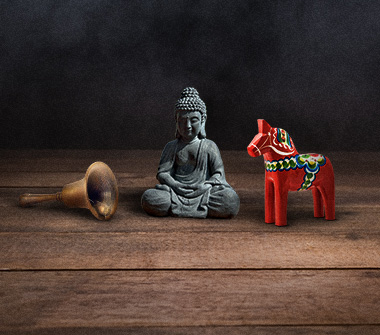 A bell, buddha statue, and wooden horse on top of table.